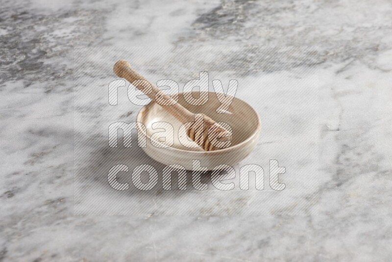 Beige pottery bowl with wooden honey dipper in it on grey marble background