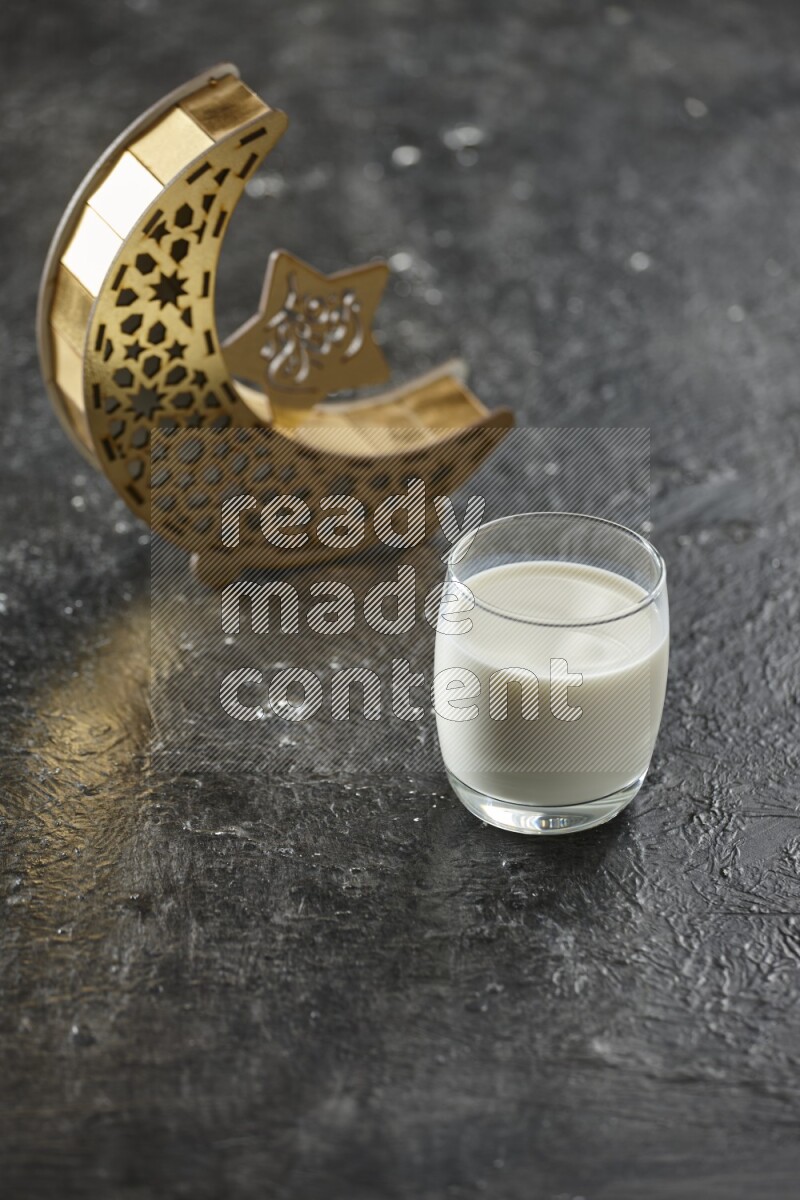 A wooden golden crescent lantern with different drinks, dates, nuts, prayer beads and quran on textured black background