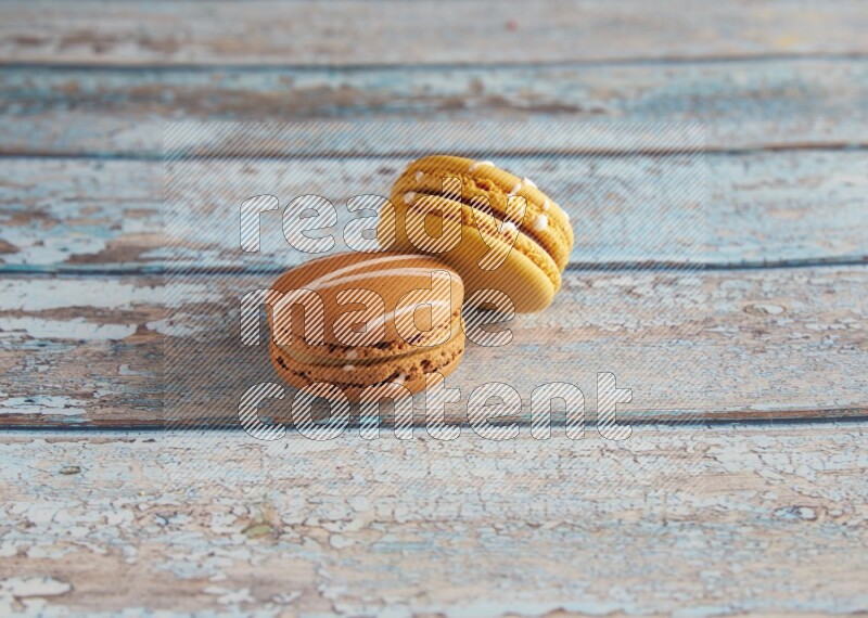 45º Shot of of two assorted Brown Irish Cream, and Yellow Piña Colada macarons on light blue background