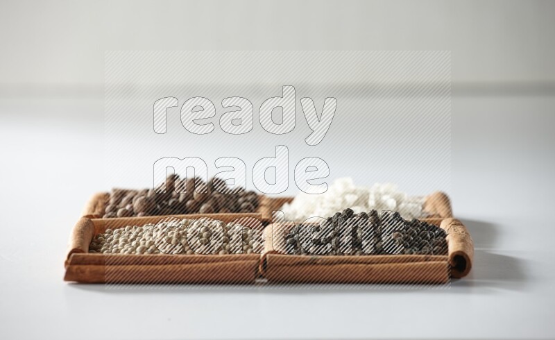 4 مربعات من أعواد القرفة ممتلئة ببهار الفلفل الحلو والملح الأبيض والفلفل الأبيض والفلفل الأسود على أرضية بيضاء