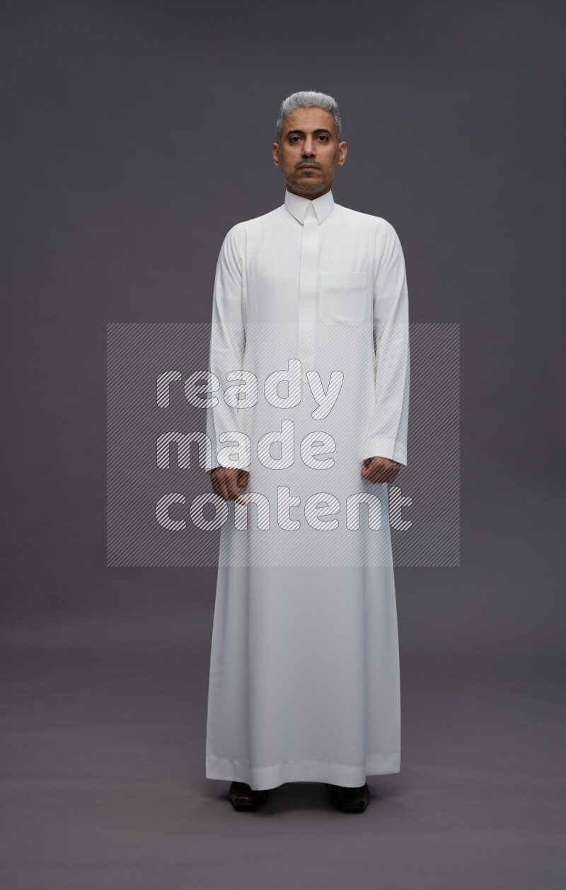 Saudi man wearing thob standing interacting with the camera on gray background