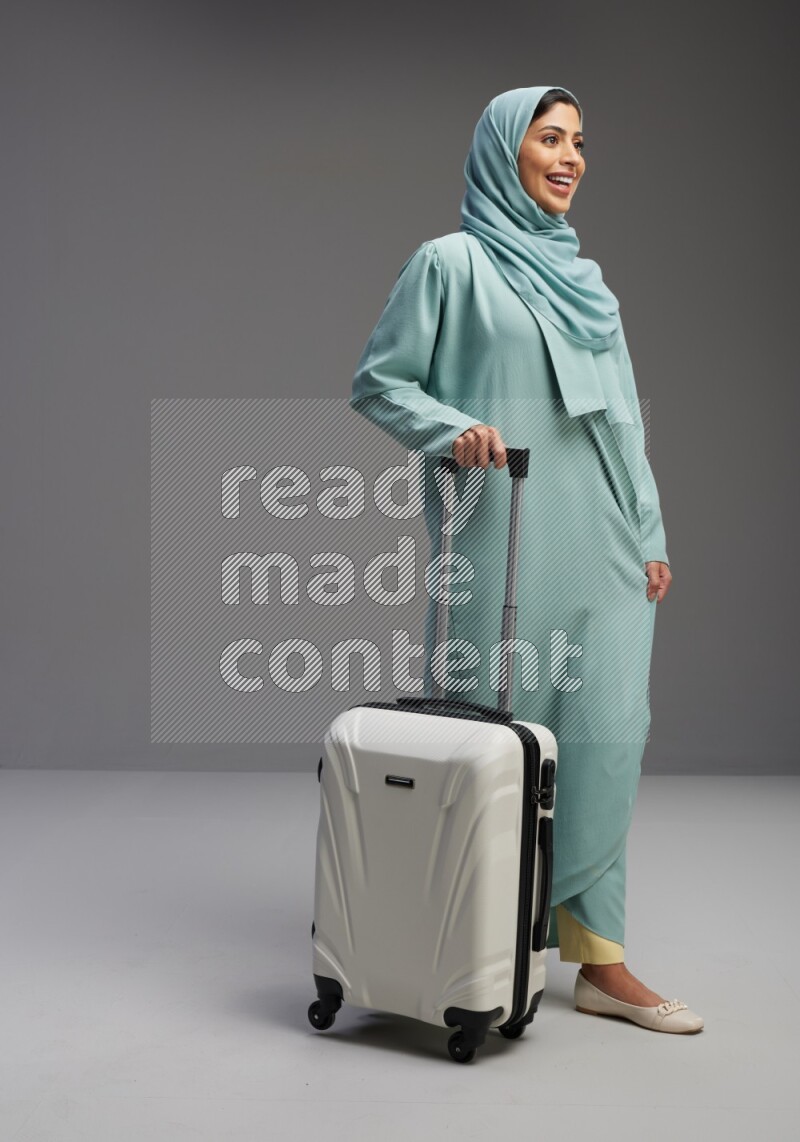 Saudi Woman wearing Abaya standing holding Travel bag on Gray background
