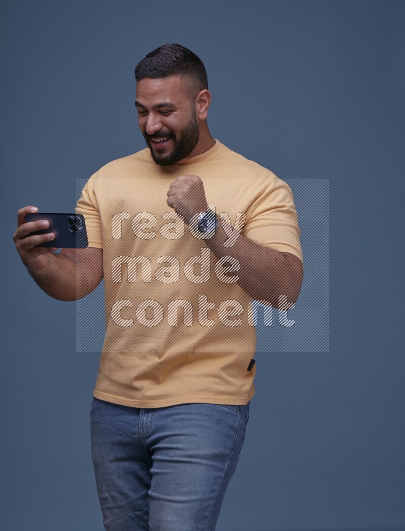 A man Playing Games on Smartphone on Blue Background wearing Orange T-shirt