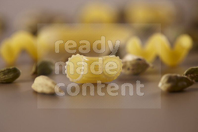 Raw pasta with different ingredients such as cherry tomatoes, garlic, onions, red chilis, black pepper, white pepper, bay laurel leaves, rosemary and cardamom on beige background
