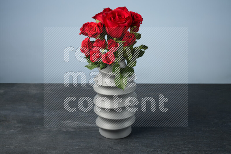 An arrangement of vivid red roses in a grey spiral vase on black marble background