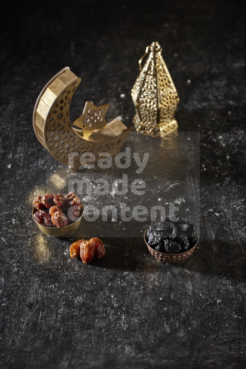 Dates in a metal bowl with dried plums beside golden lanterns in a dark setup