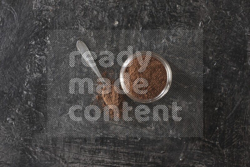 وعاء زجاجي ممتلئ ببودرة القرنفل مع ملعقة معدنية على أرضية سوداء