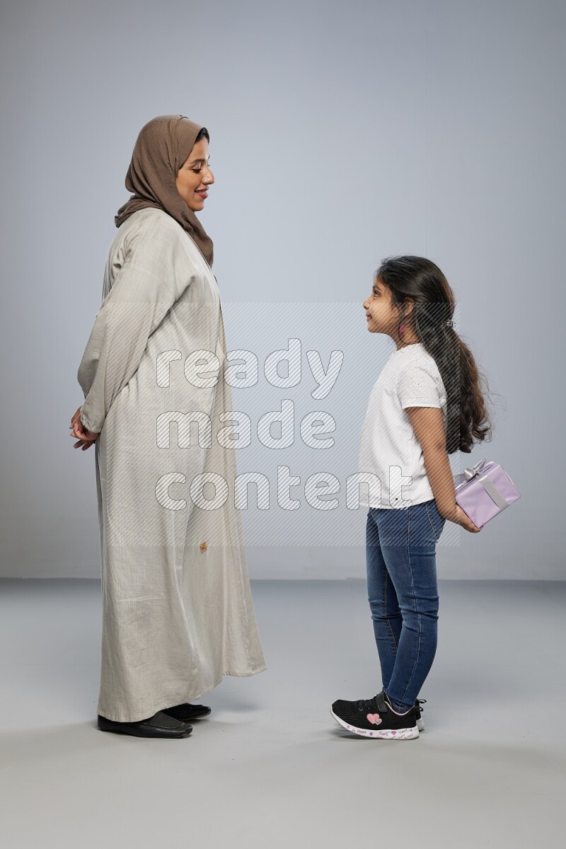 A girl standing hiding a gift behind her back for her mother on gray background