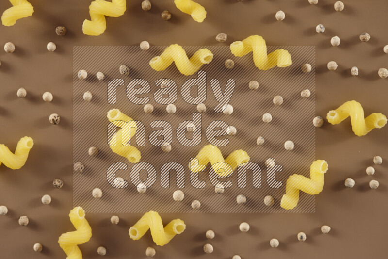 Raw pasta with different ingredients such as cherry tomatoes, garlic, onions, red chilis, black pepper, white pepper, bay laurel leaves, rosemary and cardamom on beige background
