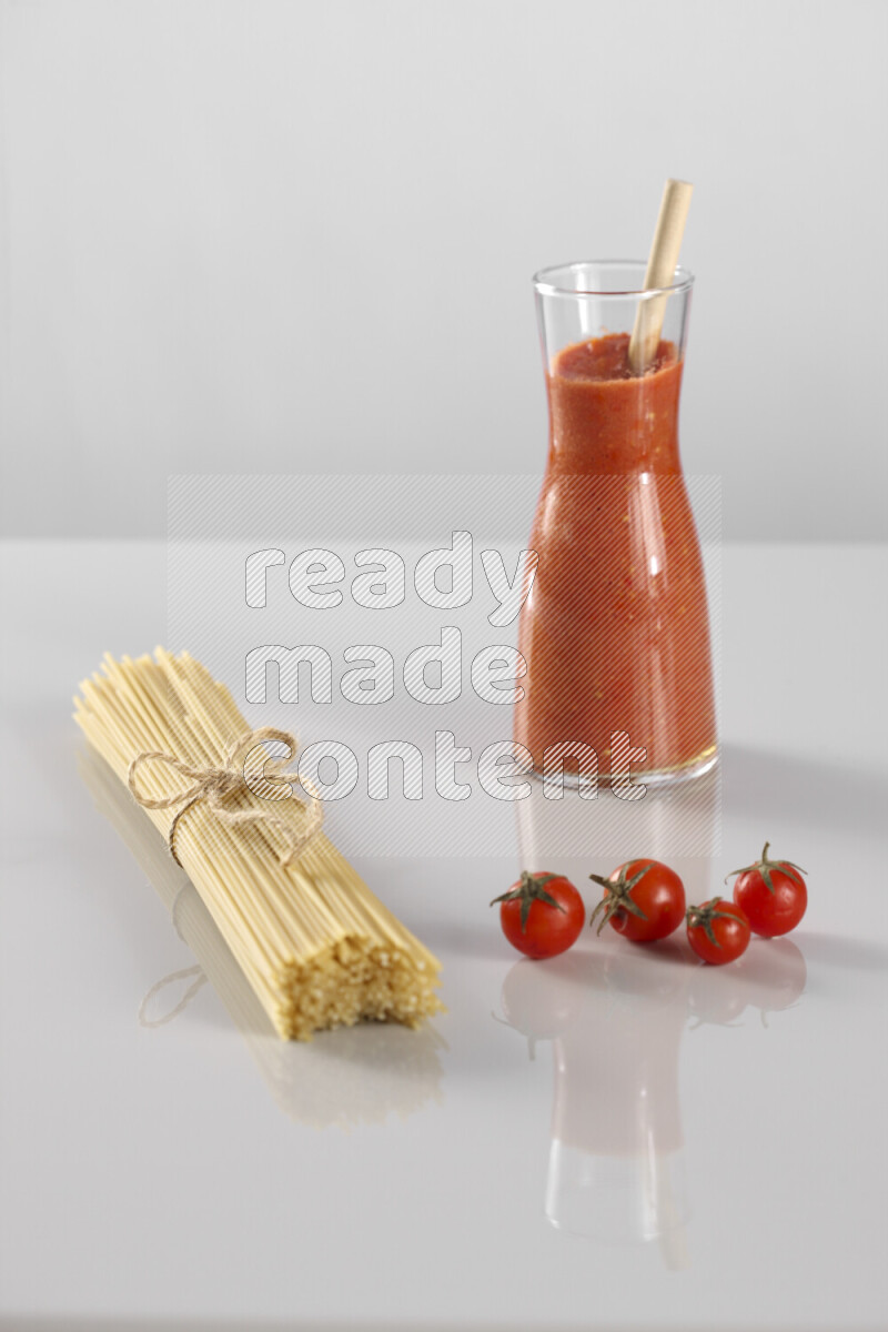 Raw pasta with tomatoe pasta with different ingredients such as cherry tomatoes, basil, garlic, bay laurel, cardamom, white pepper, black pepper, red chilis and wheat stalks on light grey background