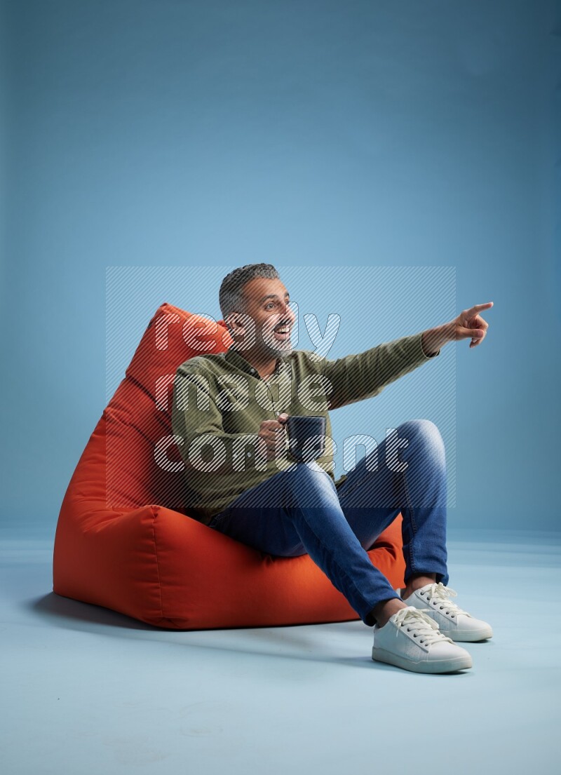 A man sitting on an orange beanbag and drinking coffee