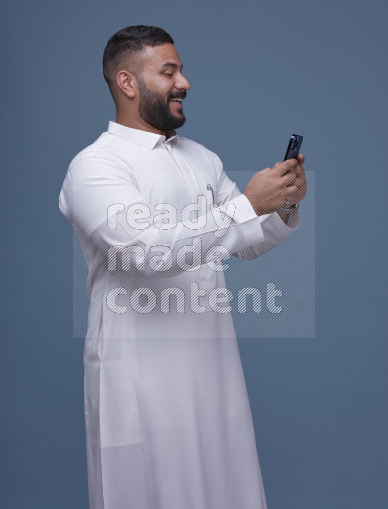 A man Texting on Blue Background wearing Saudi Thob