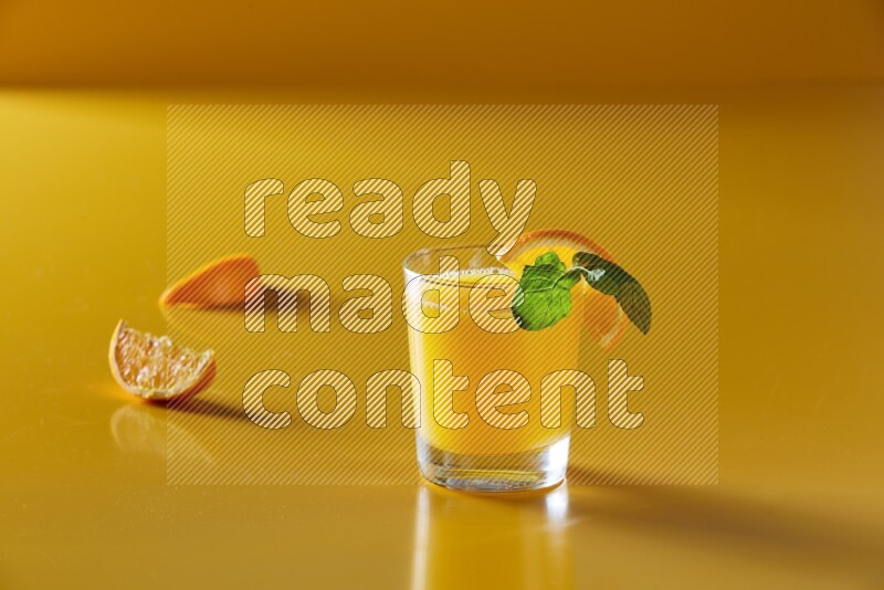 glass of orange juice with orange & mint  on yellow background