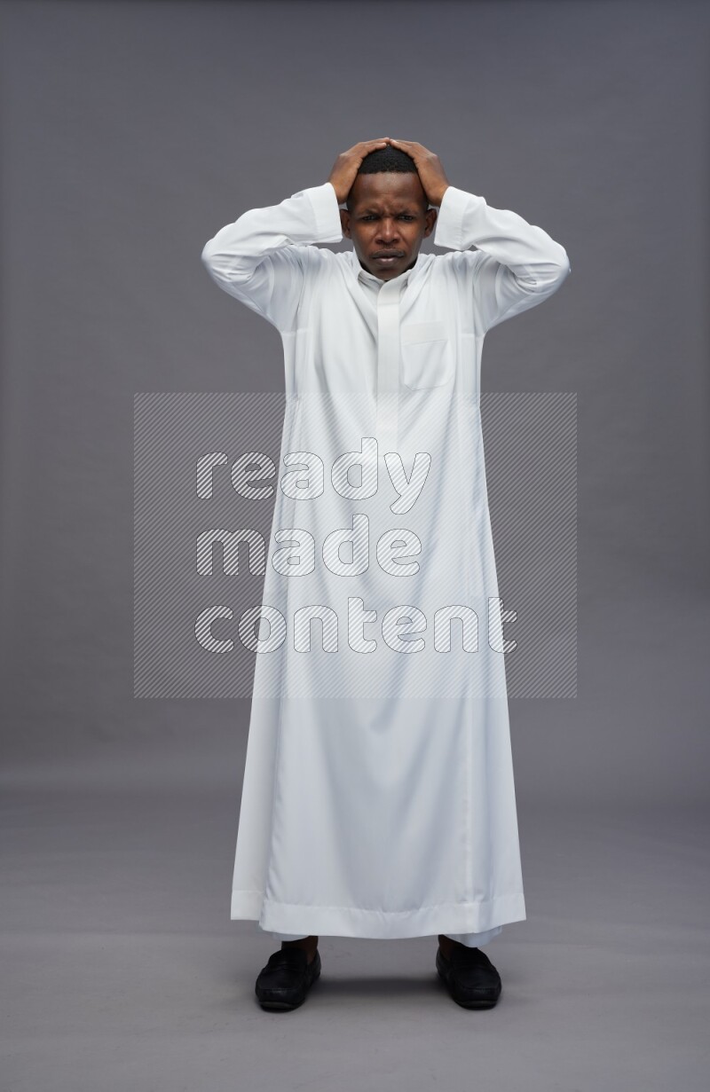 Saudi man wearing thob standing hands behind head on gray background