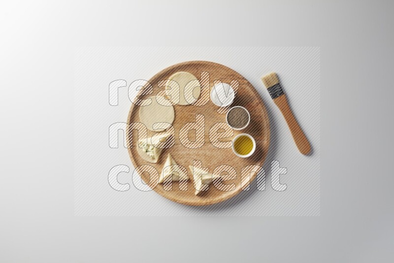two closed sambosas and one open sambosa filled with cheese while salt, black pepper and oil with oil brush aside in a wooden dish on a white background