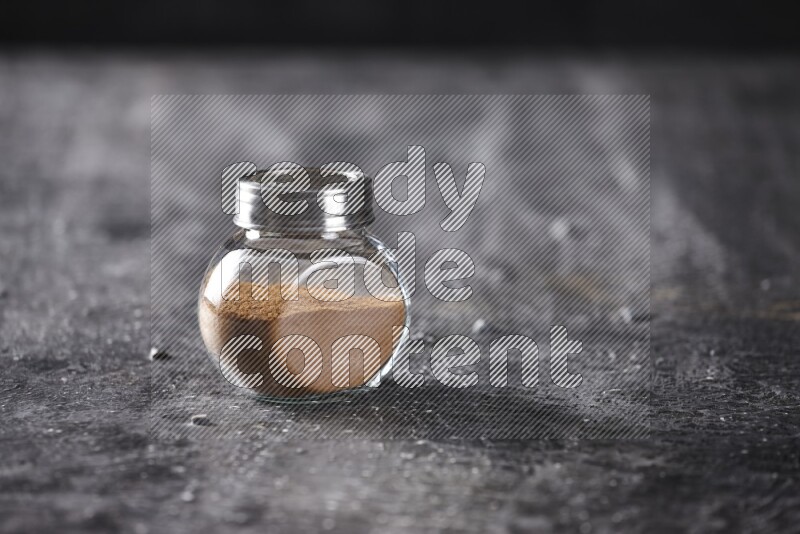 Herbal glass jar full of cinnamon powder on a textured black background