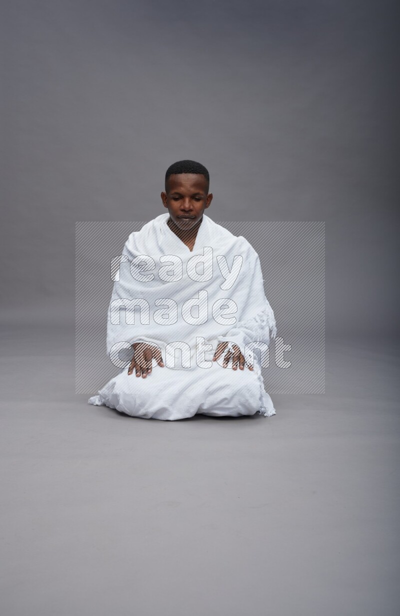 A man wearing Ehram sitting on floor praying on gray background