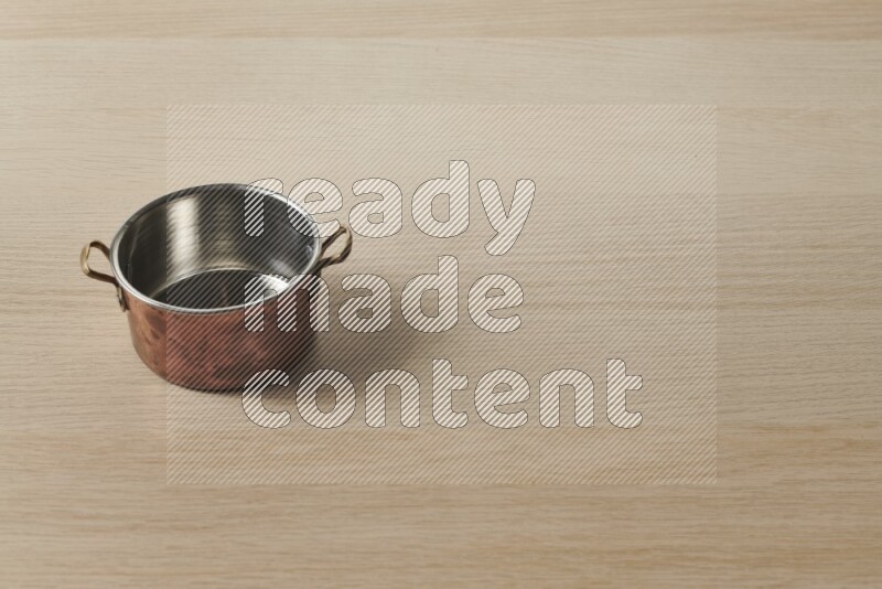 A small copper pot on light wooden background