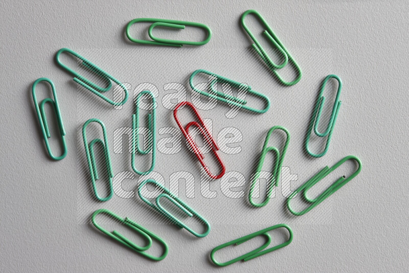 A bunch of green paper clips with a different colored paper clip in the center on grey background