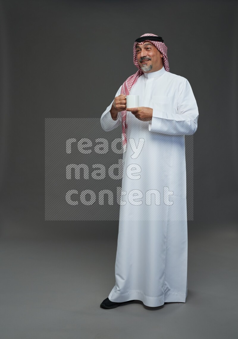 Saudi man with shomag Standing holding mug on gray background