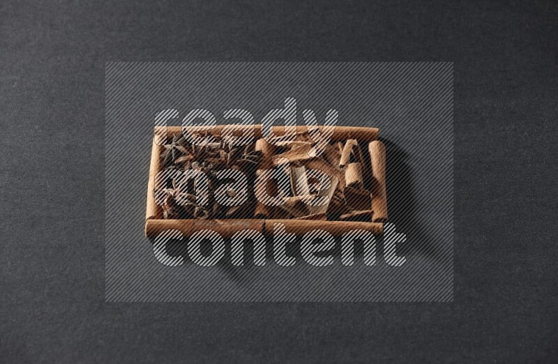 مربعان من أعواد القرفة ممتلئان باليانسون النجمي وقطع من القرفة علي خلفية سوداء