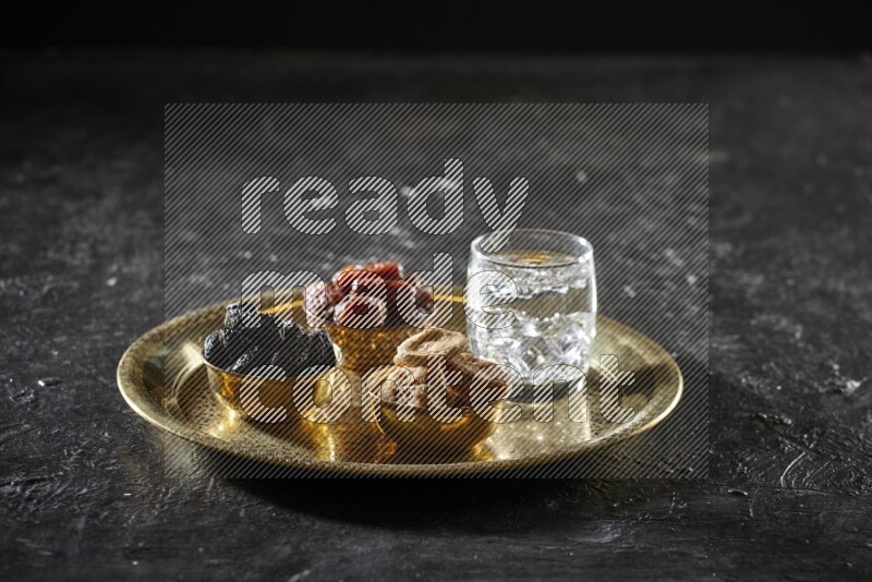 Dried fruits in metal bowls with water on a tray in dark setup