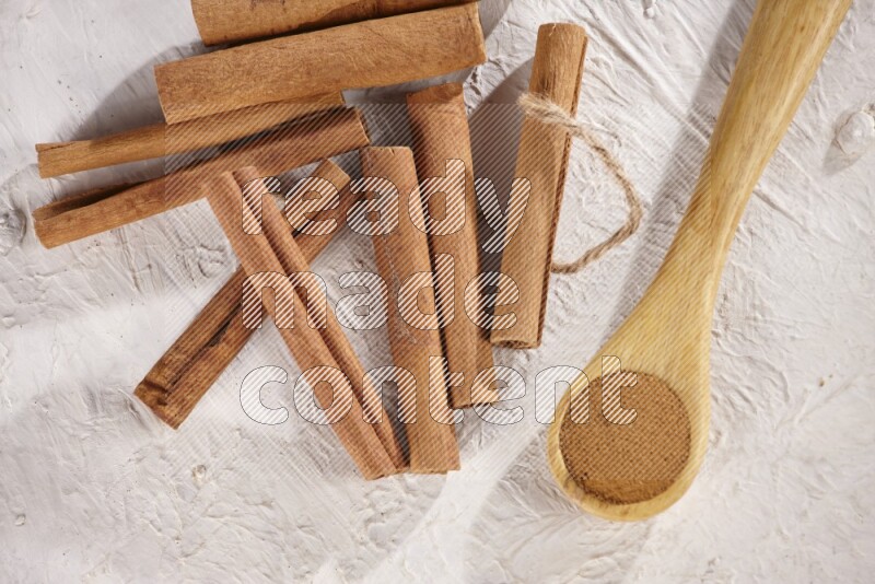 Cinnamon sticks stacked beside a wooden spoon full of cinnamon powder on white background