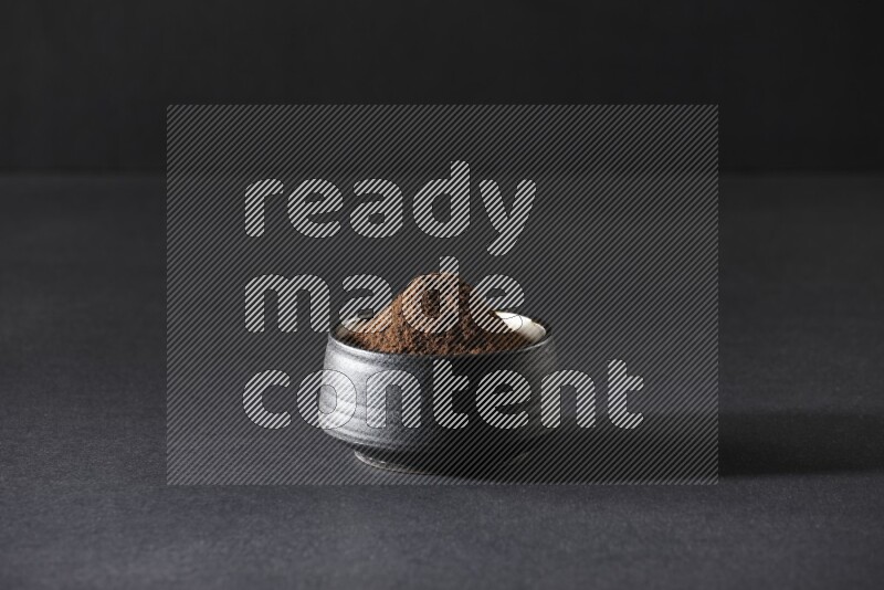 A black pottery bowl full of cloves powder on a black flooring