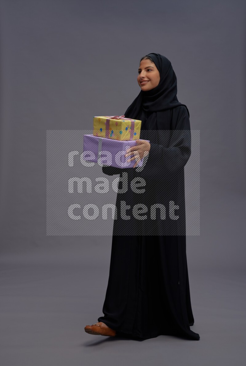 Saudi woman wearing Abaya standing holding gift box on gray background