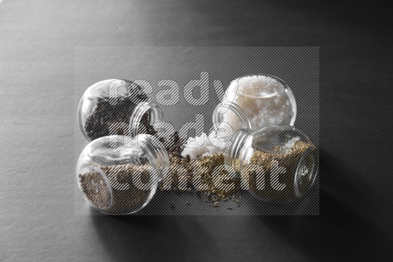 ملح وفلفل أسود وفلفل أبيض وكمون في أوعية زجاجية علي خلفية سوداء