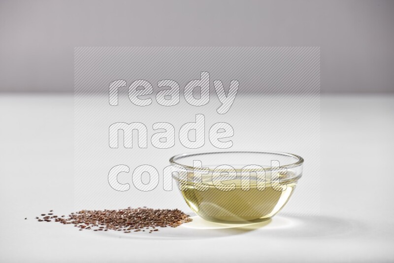 A glass bowl full of flaxseeds oil and flaxseeds beside it on a white flooring