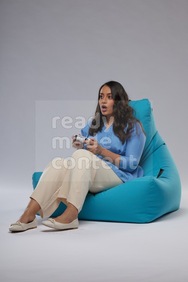A woman sitting on a blue beanbag and gaming with joystick