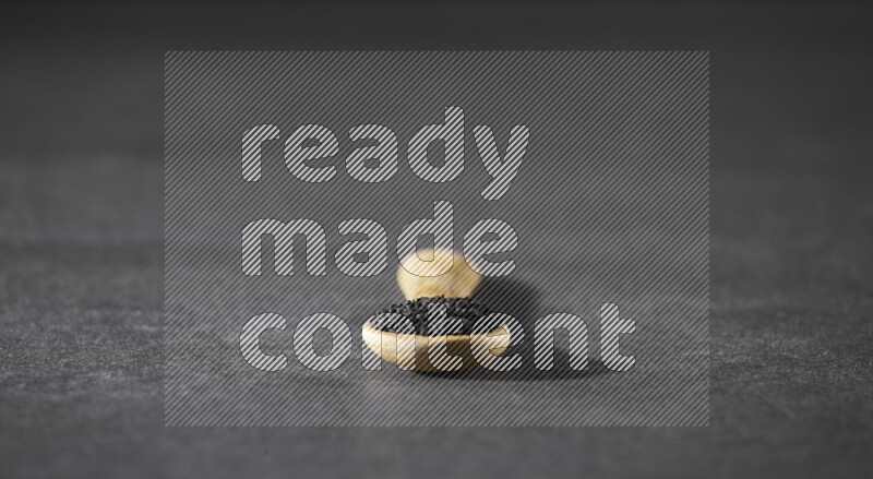 A wooden spoon full of black seeds on a black flooring