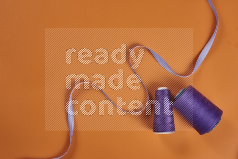 A purple collection of sewing and tailoring tools arranged on a orange background