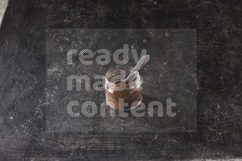 وعاء زجاجي ممتلئ ببودرة القرنفل مع ملعقة معدنية على أرضية سوداء