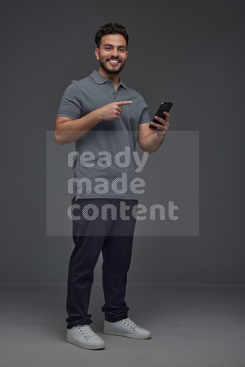 A man wearing casual standing and using his phone and making multi hand gestures eye level on a gray background