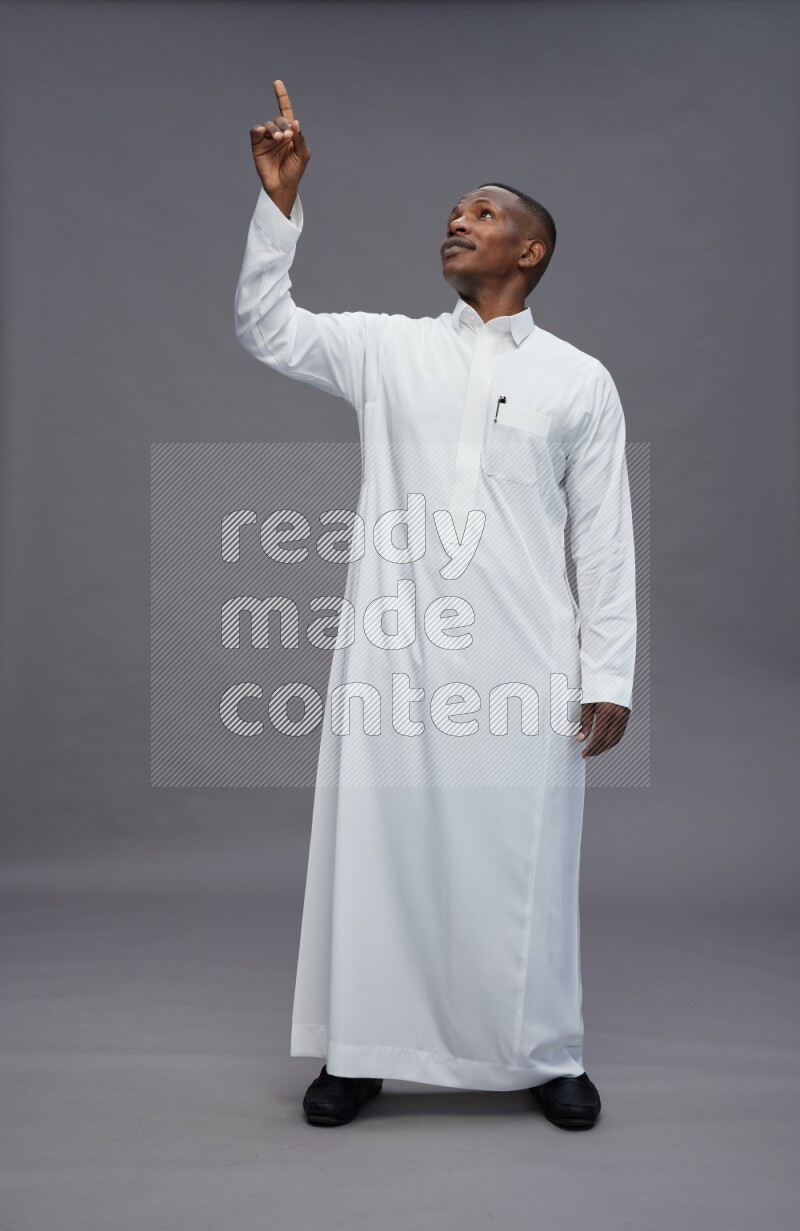 Saudi man wearing thob standing interacting with the camera on gray background
