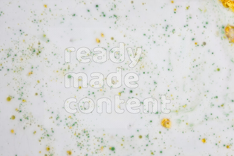 The image captures a splatter of yellow and green paint over a white backdrop