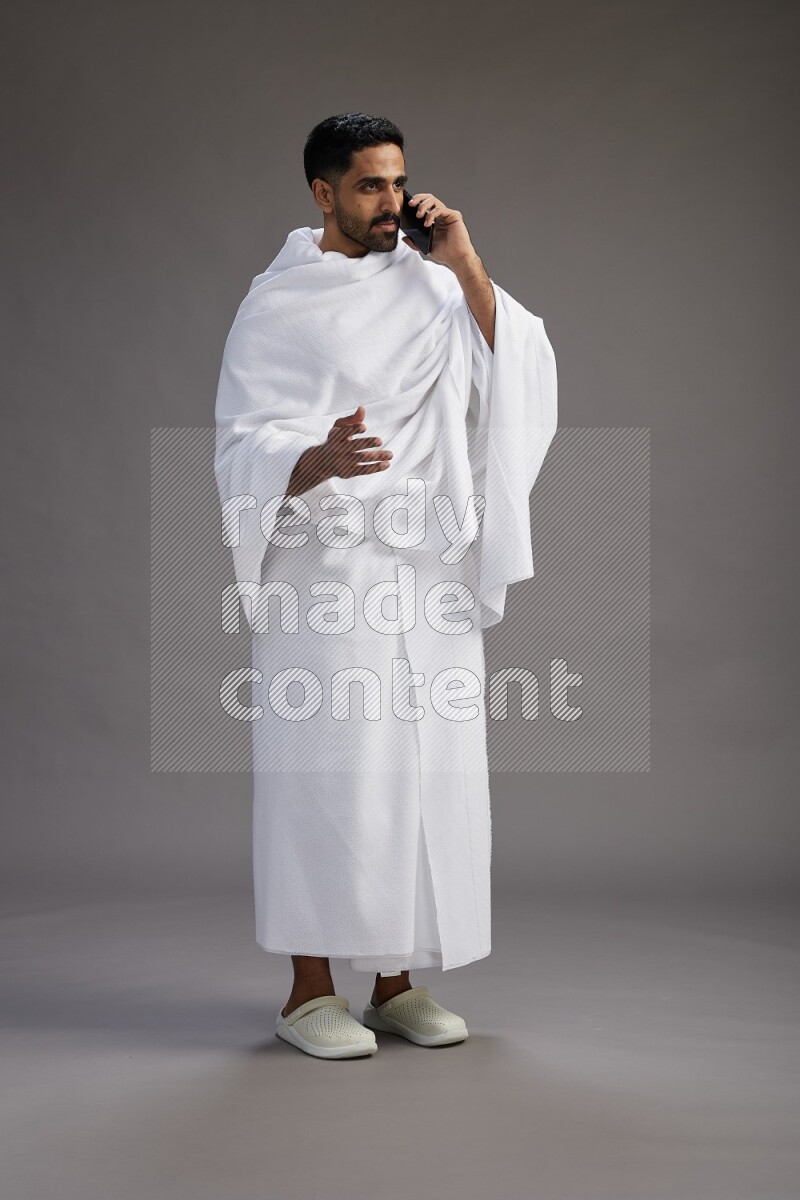 A man wearing Ehram Standing talking on phone on gray background