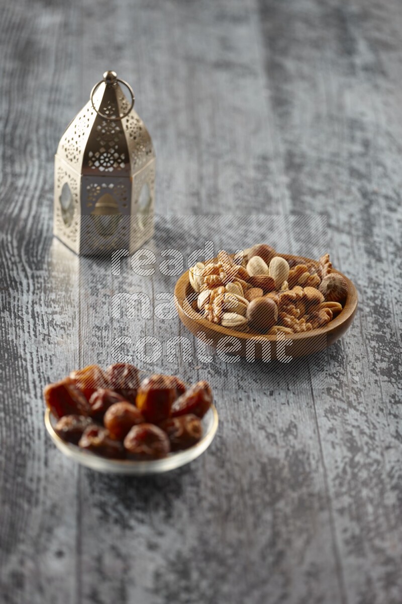 A silver lantern with different drinks, dates, nuts, prayer beads and quran on grey wooden background