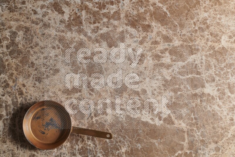 A small copper pan on beige marble background