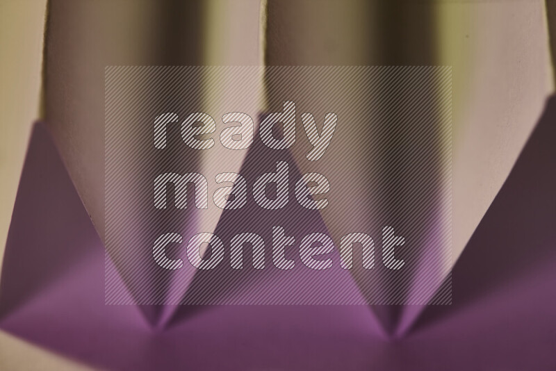 A close-up abstract image showing sharp geometric paper folds in pink gradients and warm tones