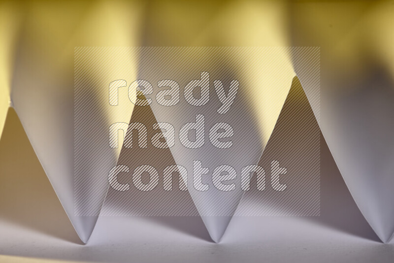 A close-up abstract image showing sharp geometric paper folds in white gradients and warm tones