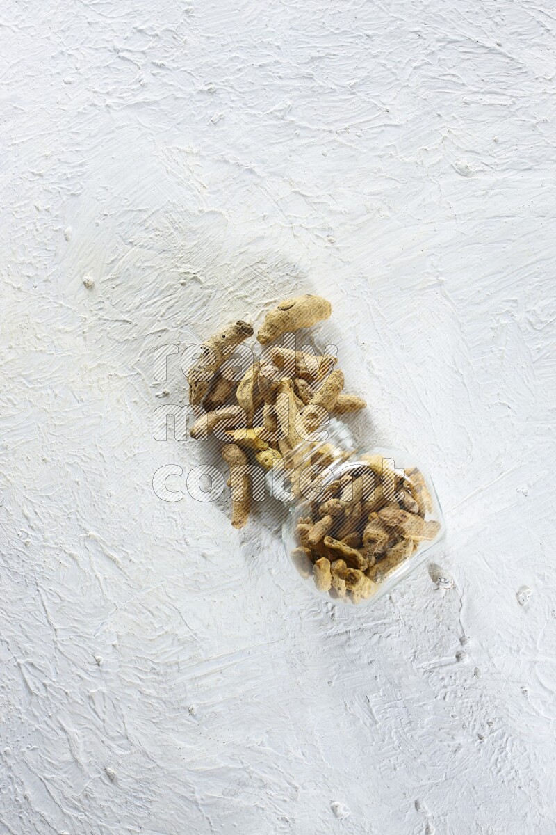 وعاء زجاجي للتوابل مقلوب وممتلئ بأصابع الكركم المجففة وتساقطت خارجه على خلفية بيضاء