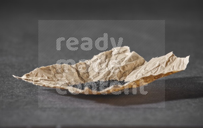 A crumpled piece of paper full of black seeds on a black flooring