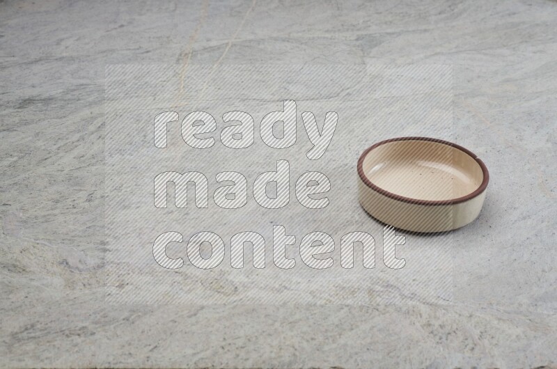A beige pottery oven bowl on grey marble background