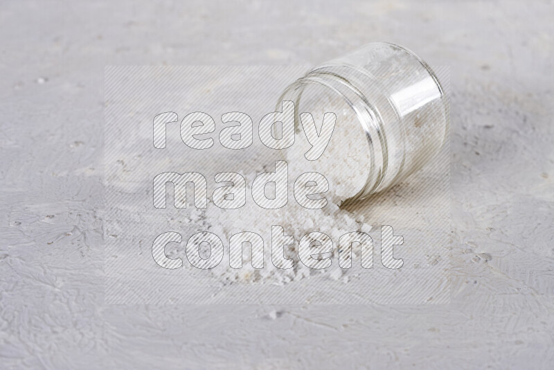 A glass jar full of coarse sea salt crystals on white background