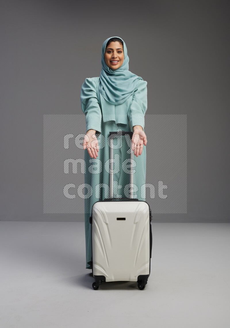 Saudi Woman wearing Abaya standing holding Travel bag on Gray background