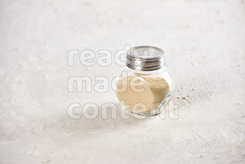 A glass jar full of ground ginger powder on white background