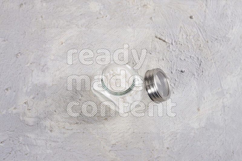 A glass jar full of coarse sea salt crystals on white background